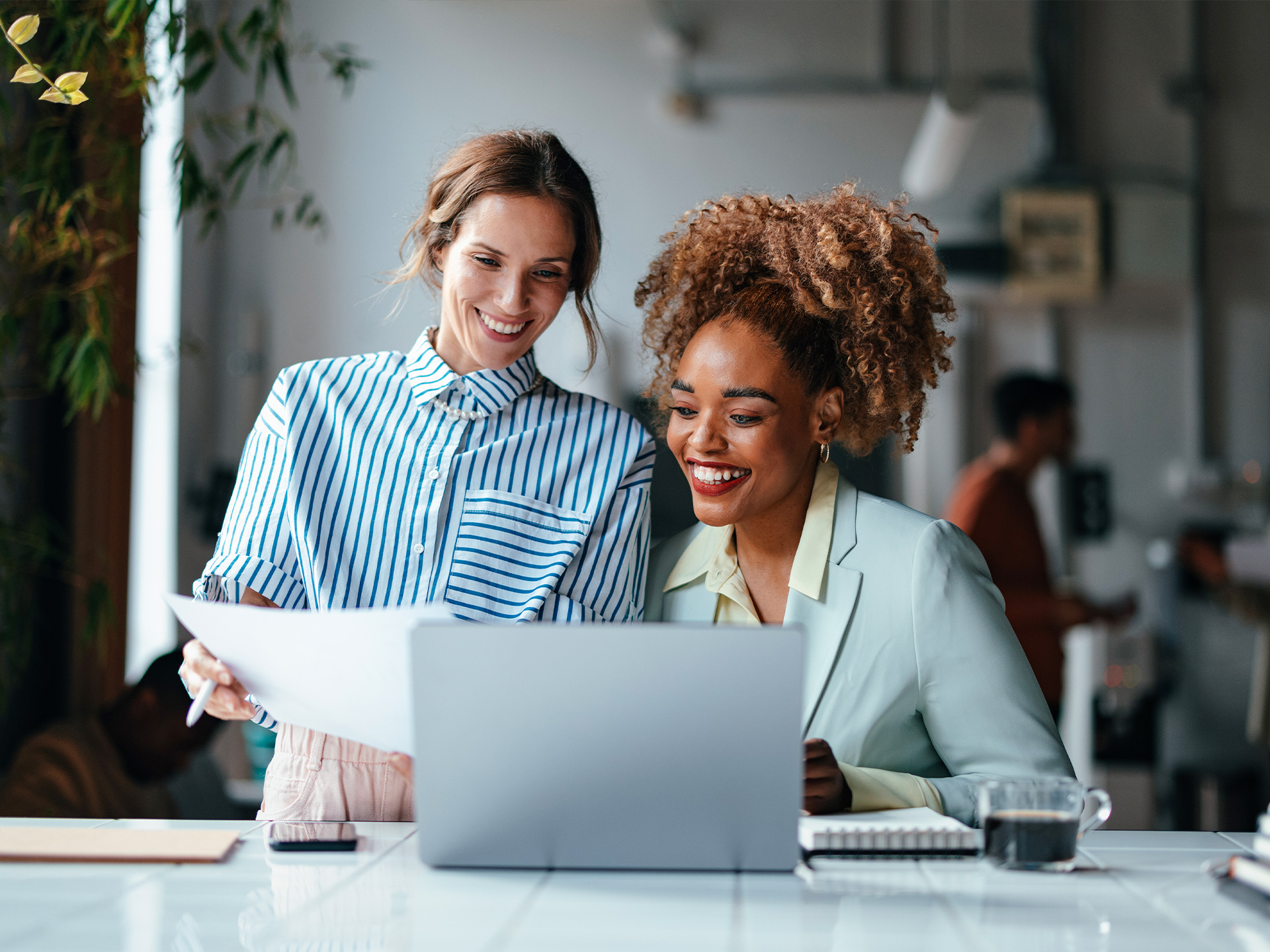 Two people working with laptop and document at desk in office