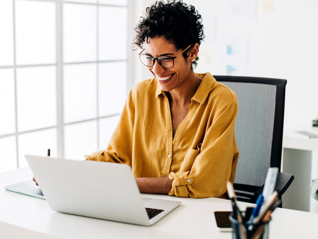 Person using laptop at desk with office supplies in bright workspace